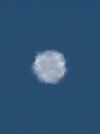 A single fluffy cloud is set against a deep blue sky, centered in the image. The cloud appears soft and slightly translucent with subtle shading indicating light and shadow.