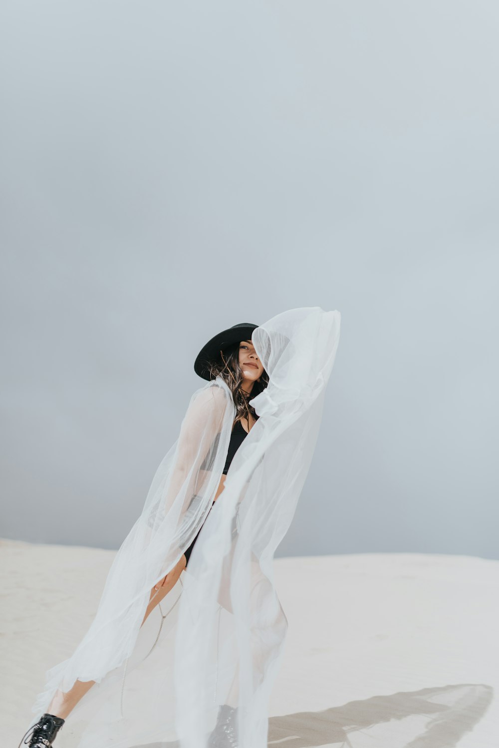 woman in white long sleeve dress and black hat standing on white sand during daytime