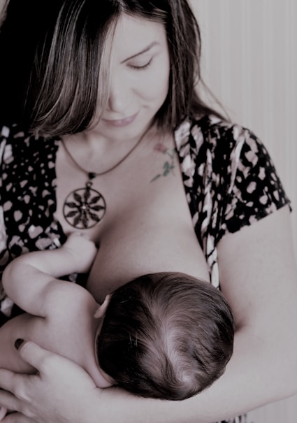 A caring nurse gently supporting a mother breastfeeding her newborn in a cozy home setting.