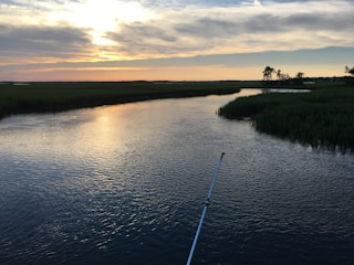 Angler casting a fishing line into a calm river surrounded by lush greenery at sunset