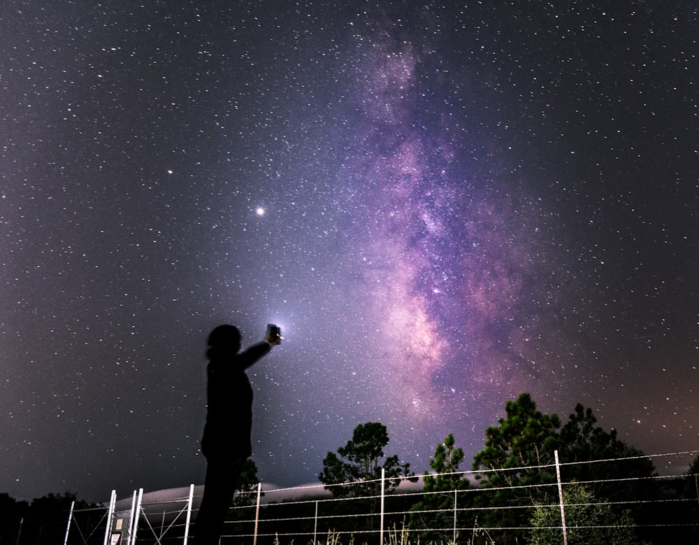 silhouette of man standing on fence under starry night