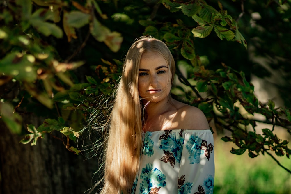 woman in blue and white floral spaghetti strap top standing near green leaves