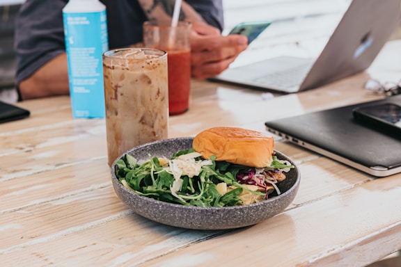 A cozy wooden table with a steaming cup of green tea, a fresh mango juice, and a sandwich on a rustic plate.