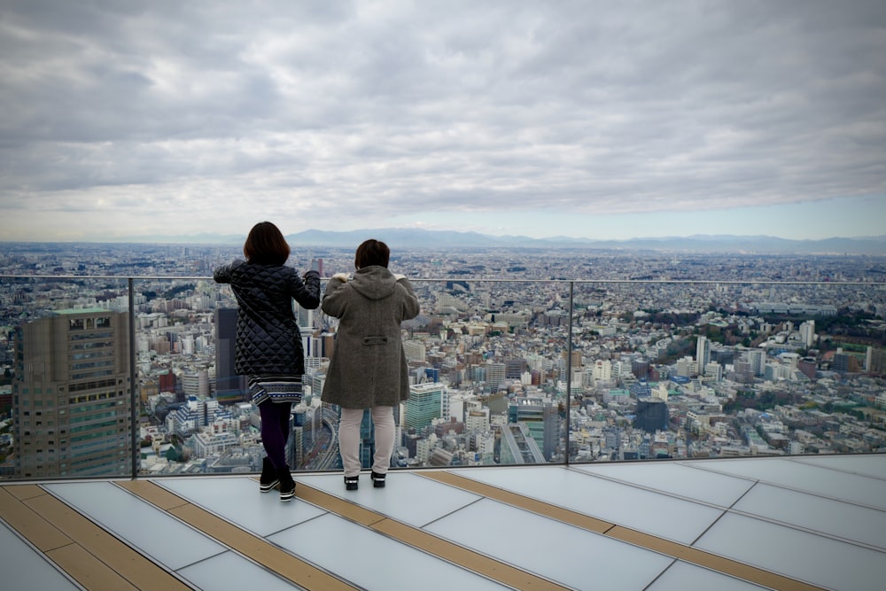 회색 재킷을 입은 남자가 낮에 도시를 바라보고 있는 건물 꼭대기에 서 있습니다.