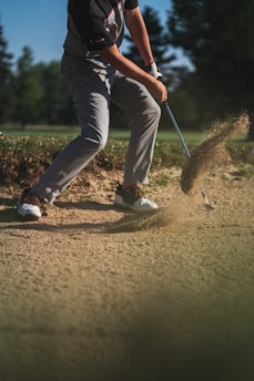 person in black t-shirt and white pants holding golf club
