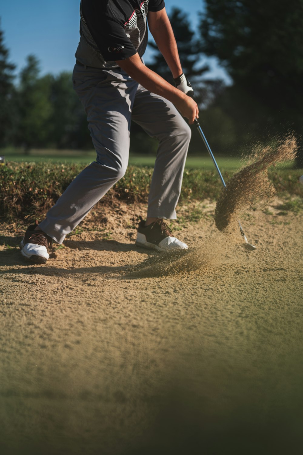 Persona in maglietta nera e pantaloni bianchi che tiene la mazza da golf