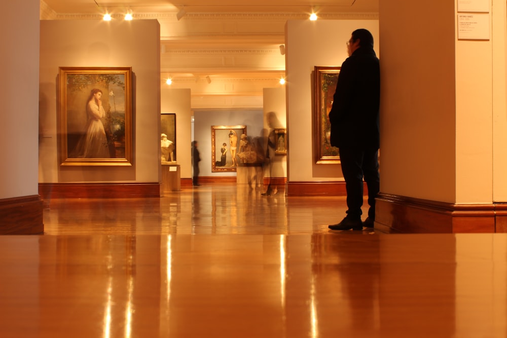 man in black jacket standing in front of paintings