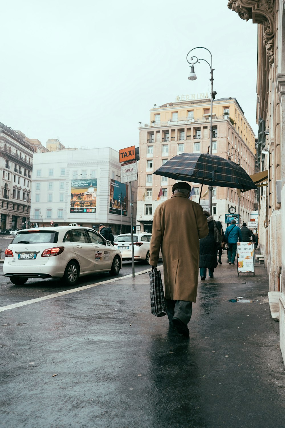 日中に歩道を歩く傘を持った茶色のコートの女性