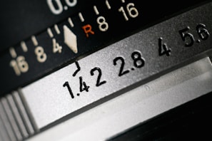 Close-up view of a camera lens aperture scale, displaying various f-stop numbers such as 1.4, 2.8, and 5.6. The R marking and a series of numerical indicators provide exposure settings.