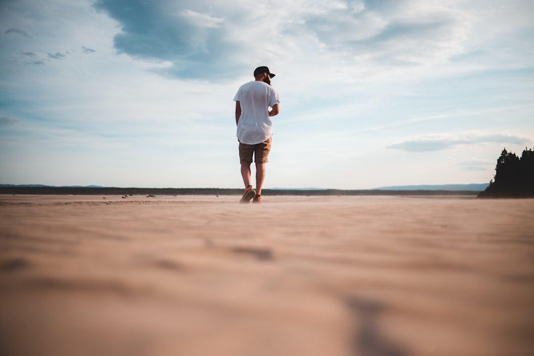man in white t-shirt and brown shorts standing on brown sand during daytime
