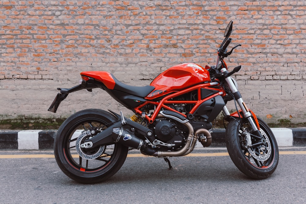 red and black motorcycle parked beside brown brick wall