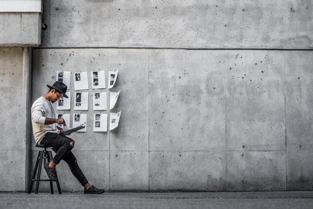 man in black jacket and black pants sitting on concrete wall