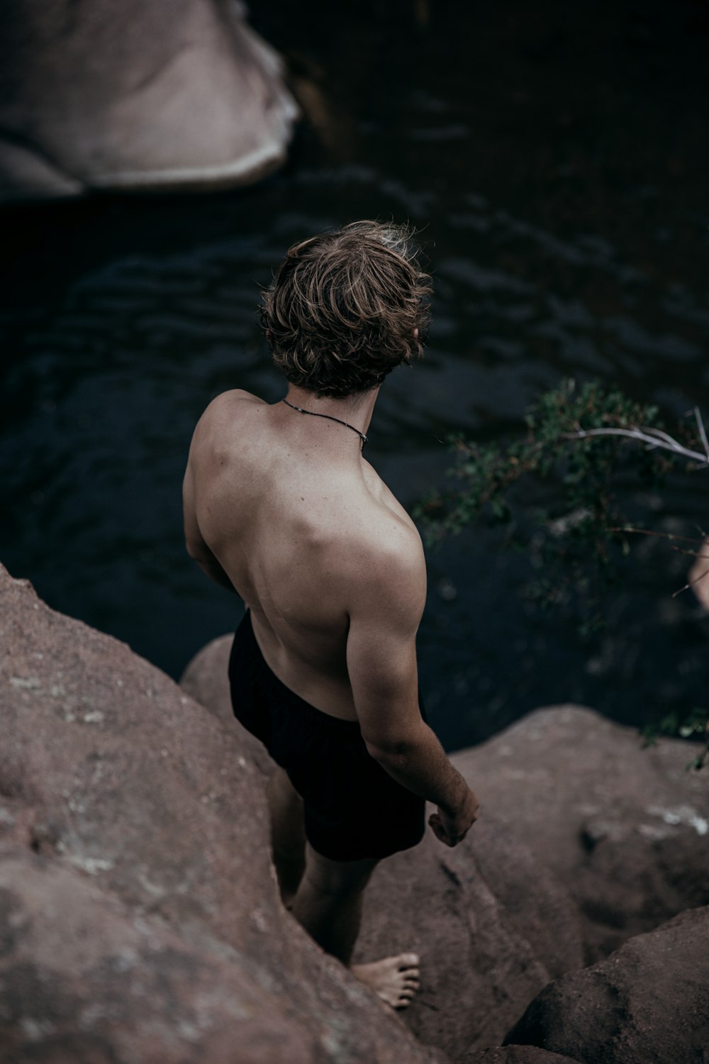 topless man in black shorts standing on rock near body of water during daytime