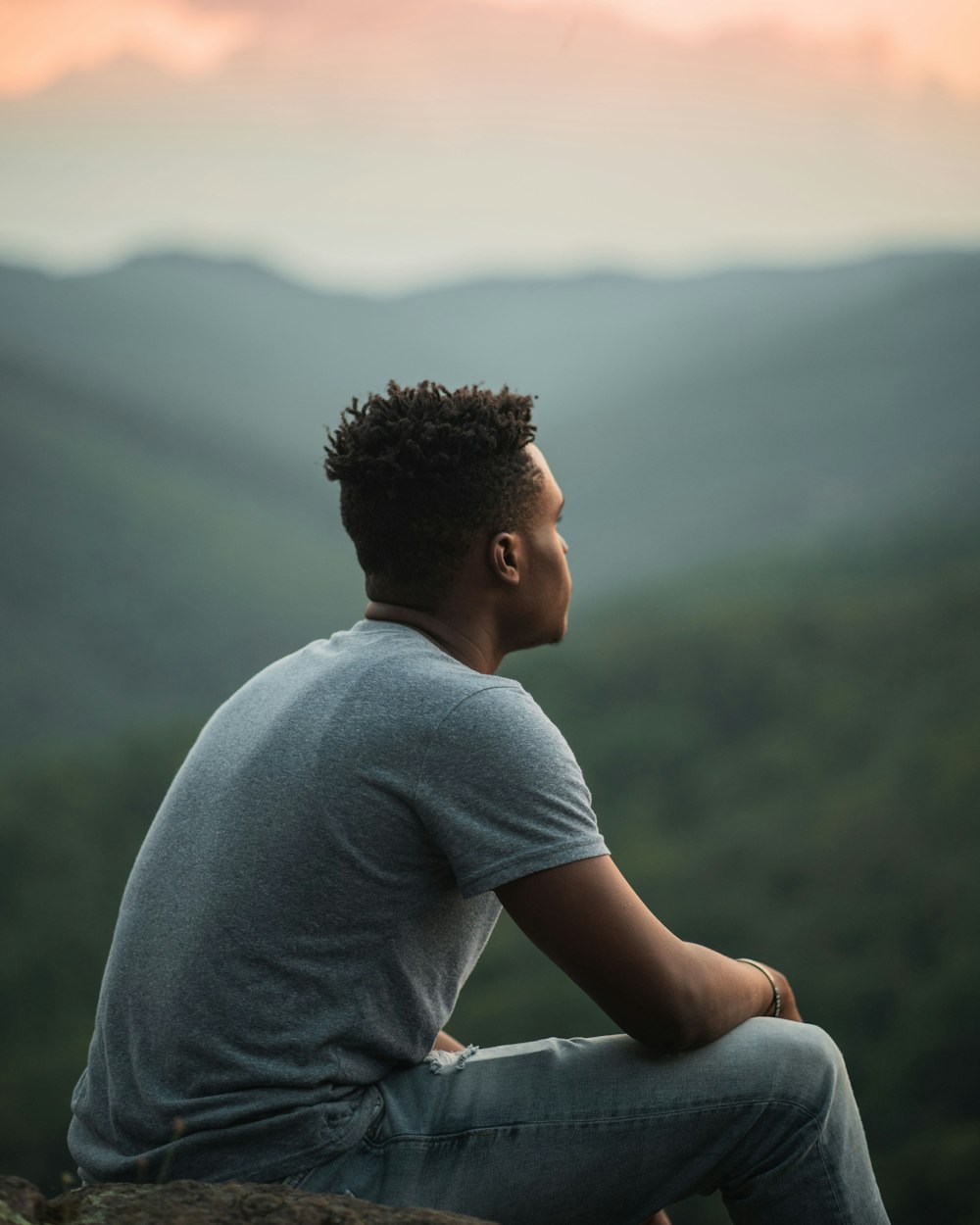 man in gray crew neck t-shirt sitting on gray rock during daytime