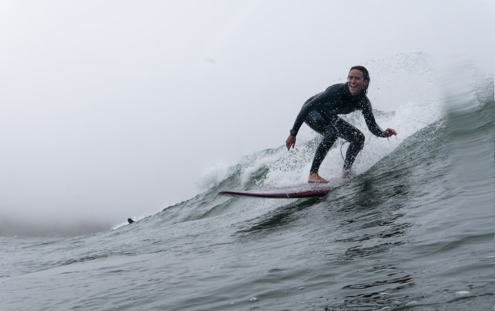 man in black wet suit riding on red surfboard on sea waves during daytime