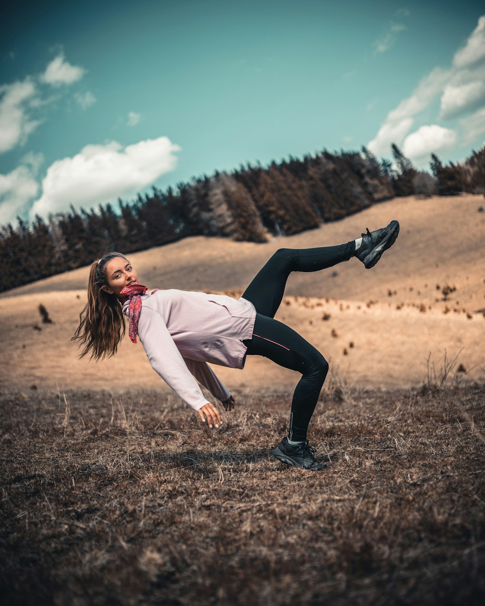 woman in white long sleeve shirt and black pants jumping on brown grass field during daytime