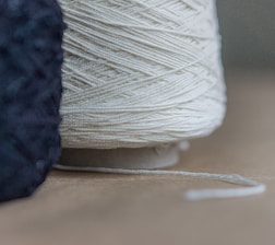 Two spools of thread with one being white and the other black. The white thread spool is prominently in the foreground, with the black thread spool partially visible on the left. The texture of the threads is clearly visible.