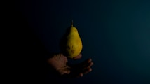 A pear is levitating against a dark background with a hand visible underneath, creating a sense of balance and suspension.