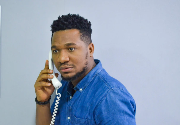 man in blue denim button up shirt holding white phone