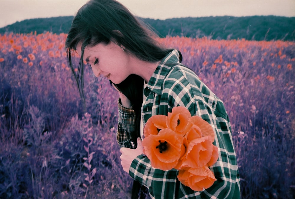 woman in black and white plaid long sleeve shirt holding orange flower