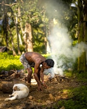 man in white and black checkered shirt sitting on ground with white short coated dog during