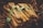 A collection of intricately crafted wooden kitchen utensils, neatly stacked and adorned with green tags. The utensils display rich wood grain patterns with a natural, polished finish.