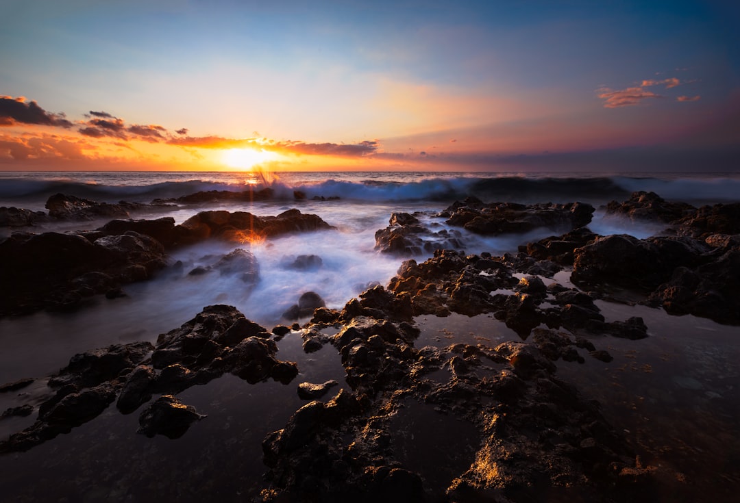 black rock formation on sea during sunset