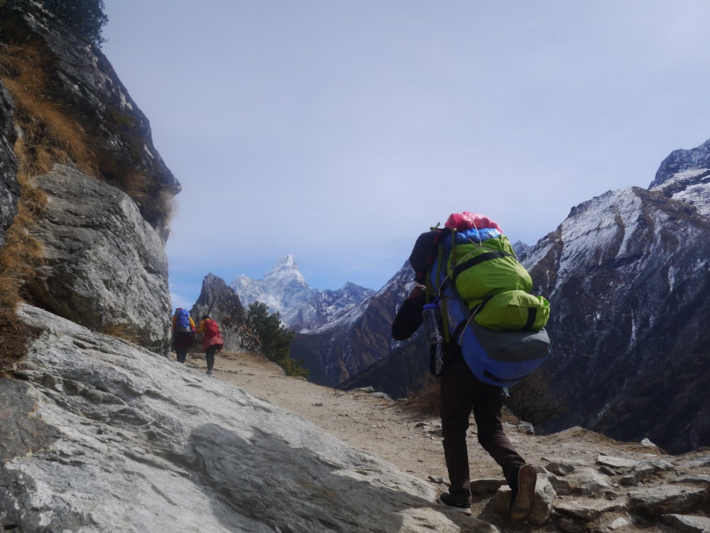 man in green jacket and black pants with hiking backpack walking on rocky mountain during daytime