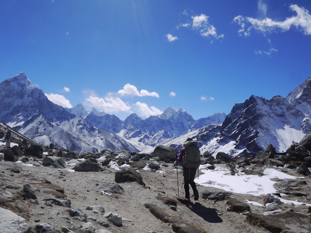 person standing on rocky ground near snow covered mountains under blue sky during daytime