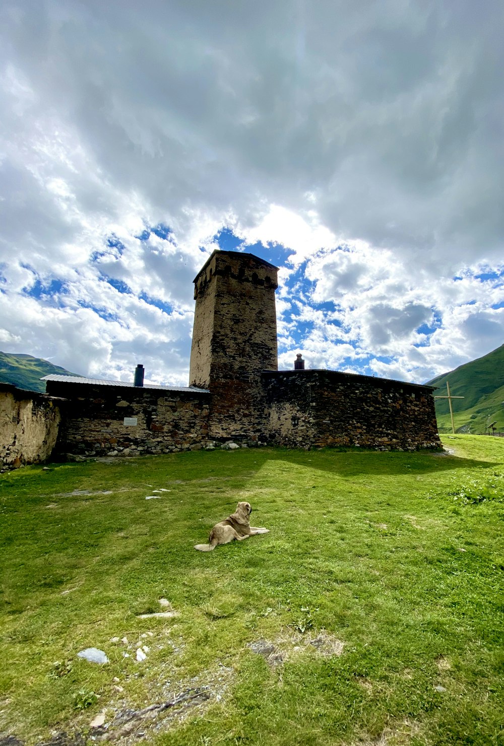 Edificio de ladrillo marrón en campo de hierba verde bajo cielo azul y nubes blancas durante el día