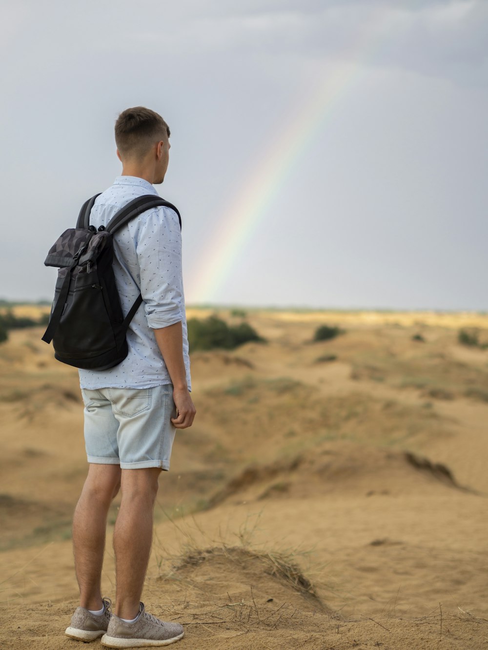 man in blue denim jacket and white shorts standing on brown field during daytime