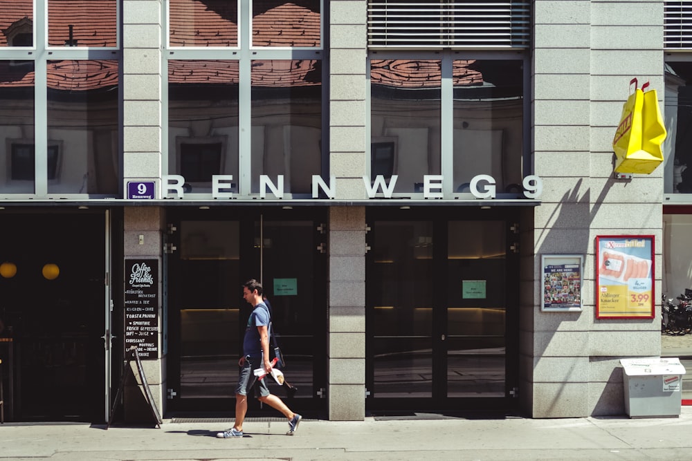 man in blue t-shirt and blue denim shorts walking on sidewalk near brown and white