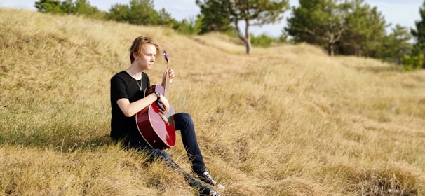 A musician playing a guitar outdoors, surrounded by nature.
