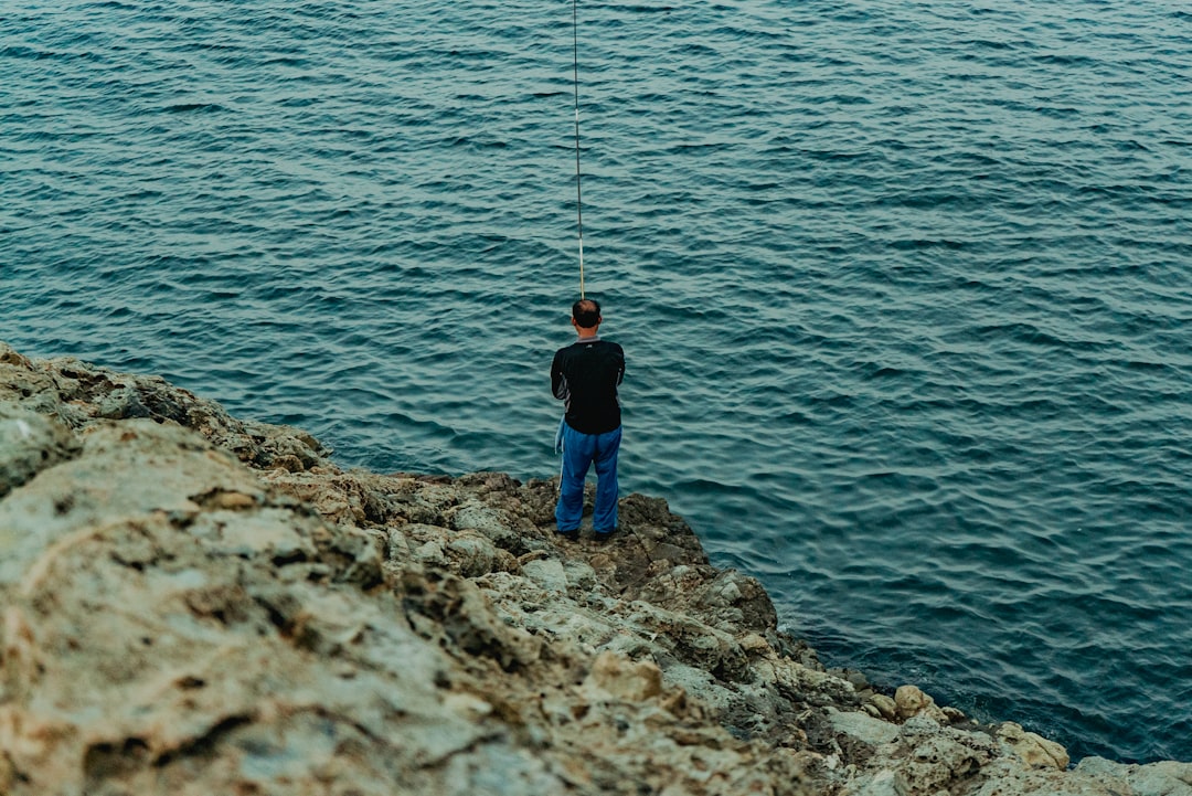 boy in black jacket and blue denim jeans fishing on sea during daytime
