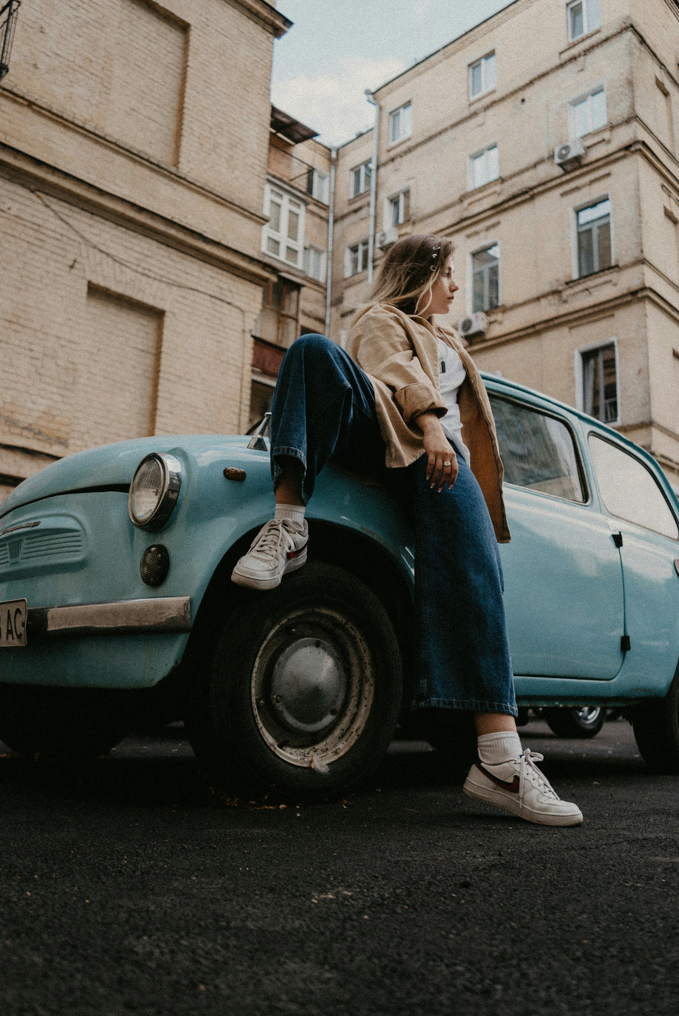 woman in blue denim jeans leaning on blue car