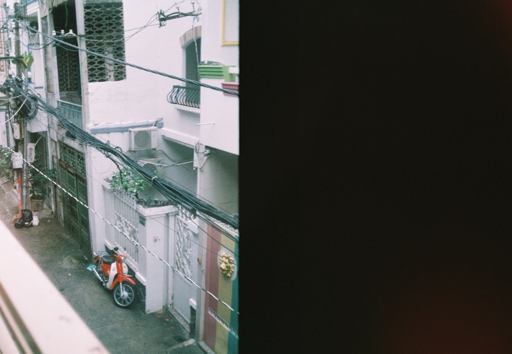 red and black motorcycle parked beside white concrete building during daytime