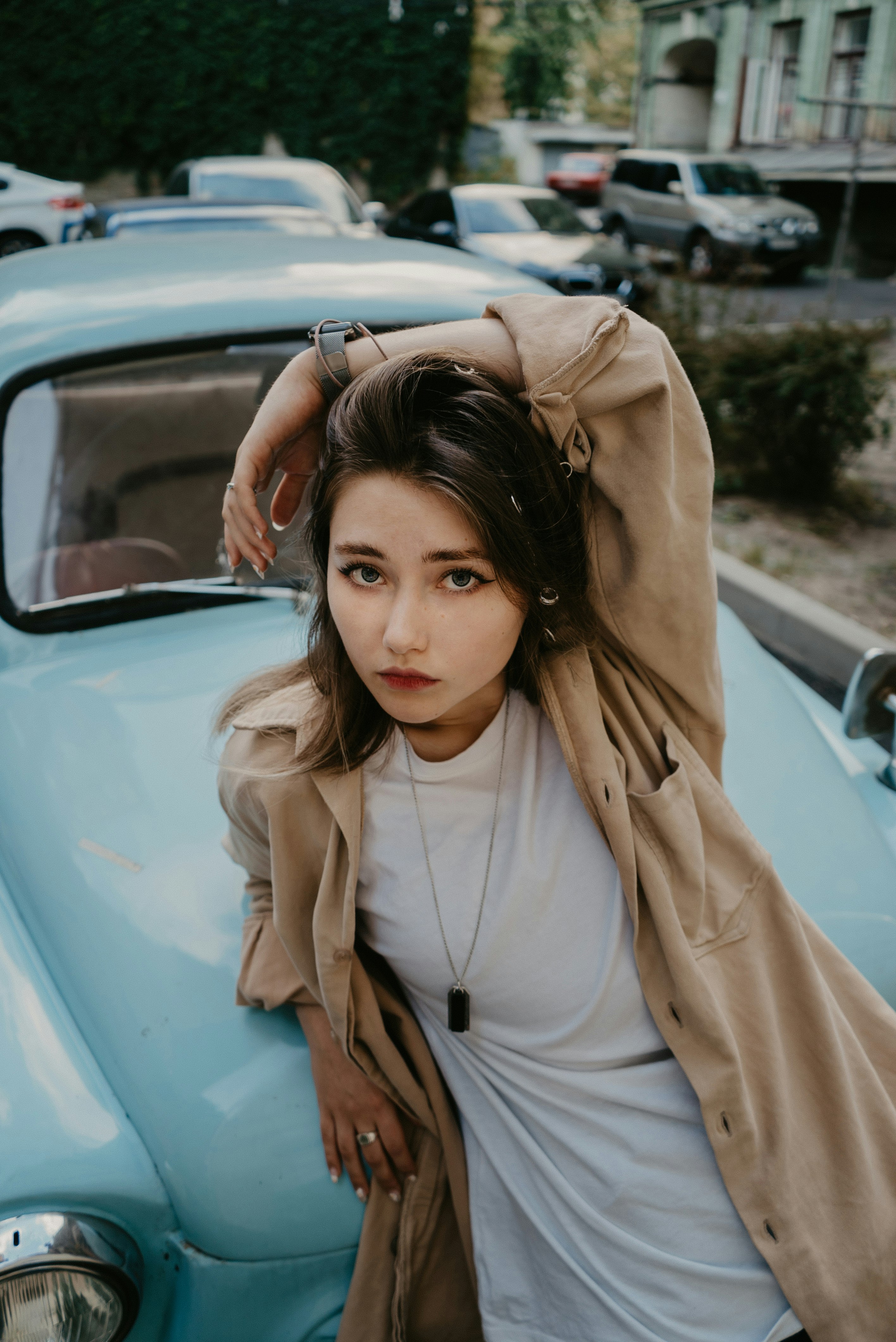 woman in beige coat leaning on blue car