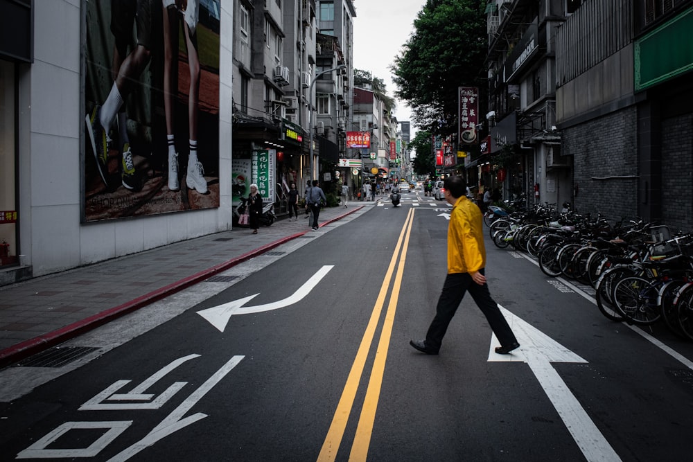 man in yellow jacket and black pants walking on pedestrian lane during daytime