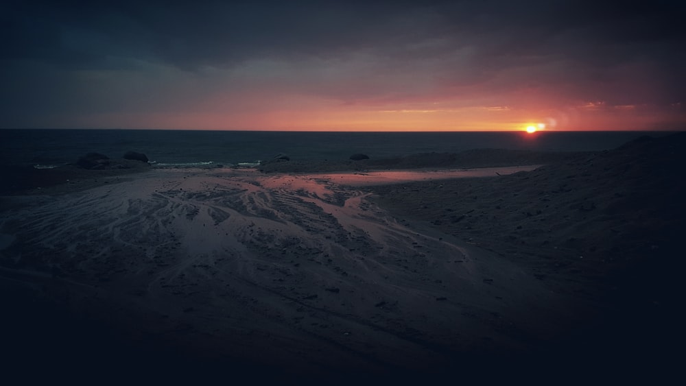 the sun is setting over a sandy beach