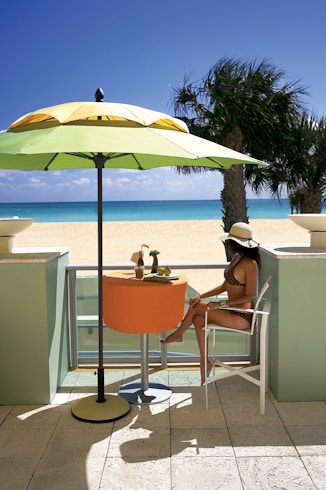 woman in white tank top sitting on orange chair under blue umbrella during daytime