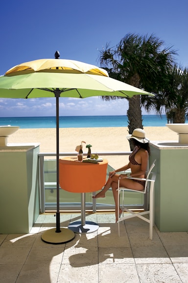 woman in white tank top sitting on orange chair under blue umbrella during daytime