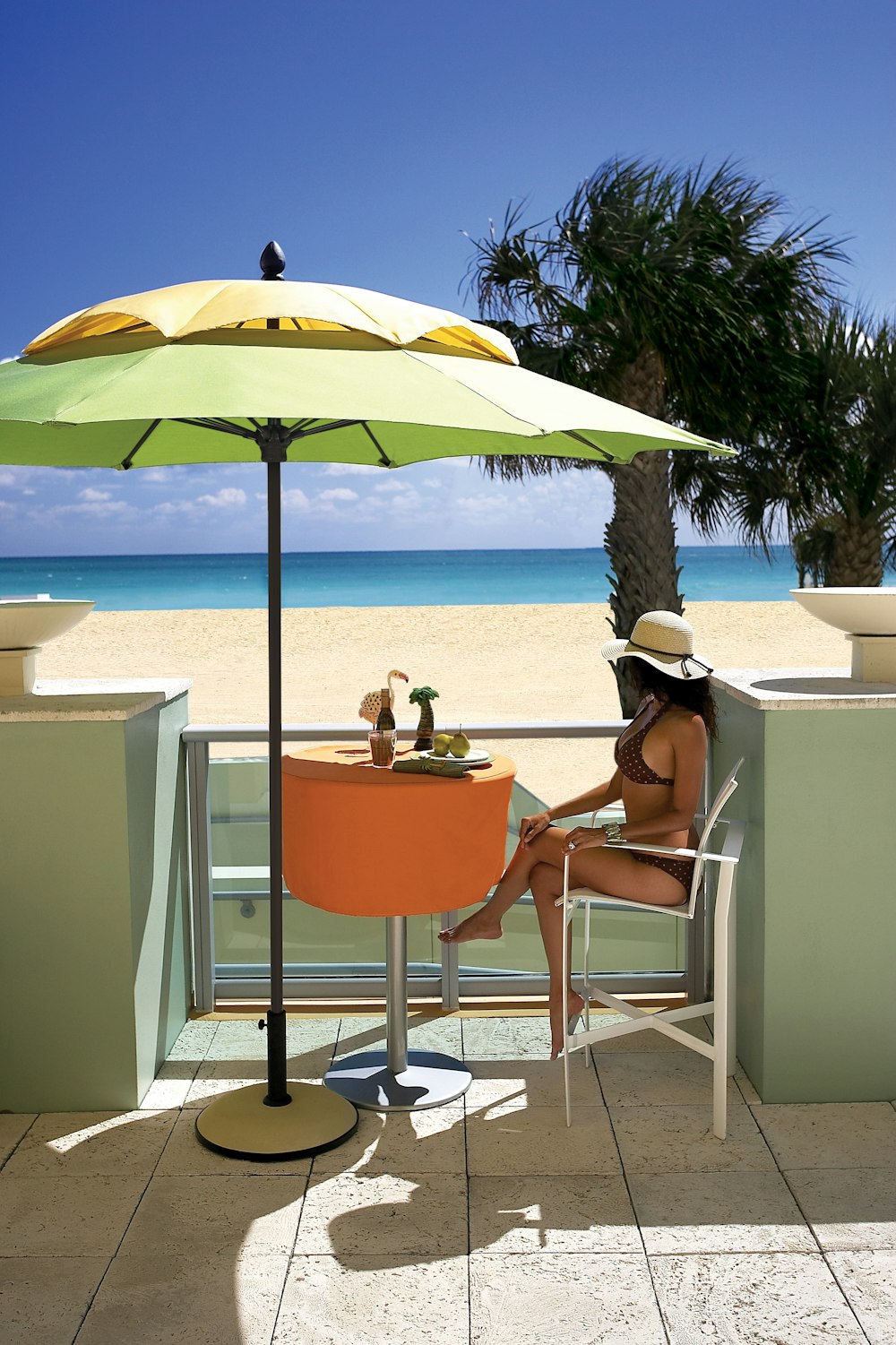 woman in white tank top sitting on orange chair under blue umbrella during daytime