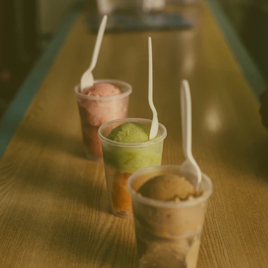 Close-up of colorful rolled ice cream cups topped with fresh fruit and chocolate drizzle on a wooden counter.
