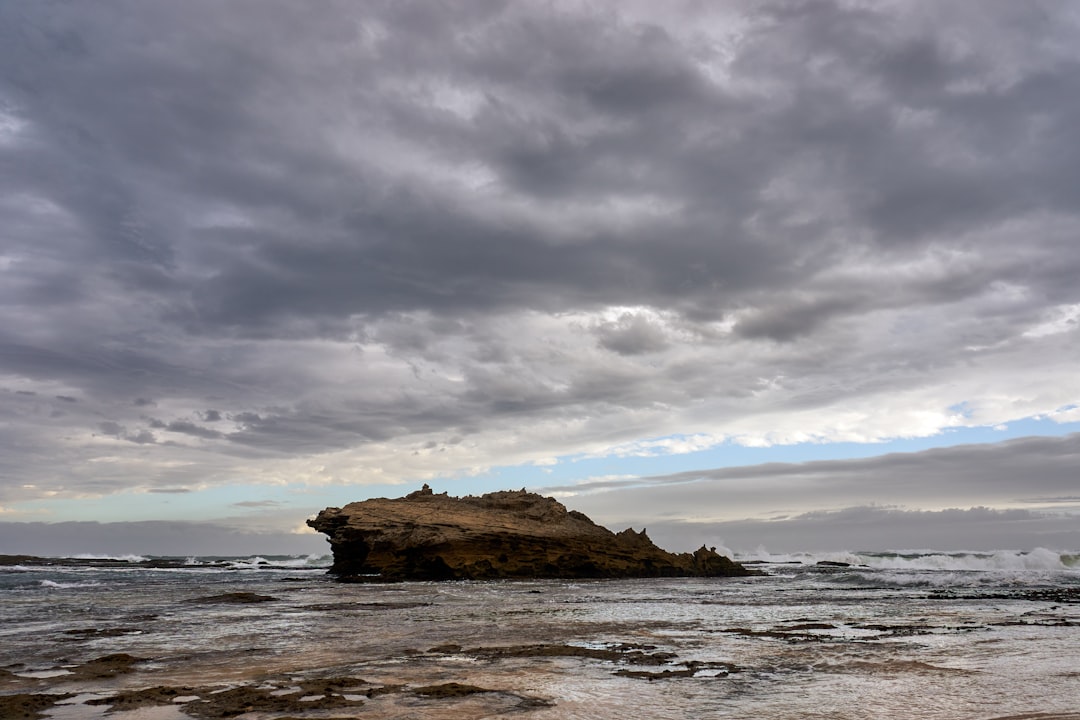 brown rock formation on sea under gray clouds