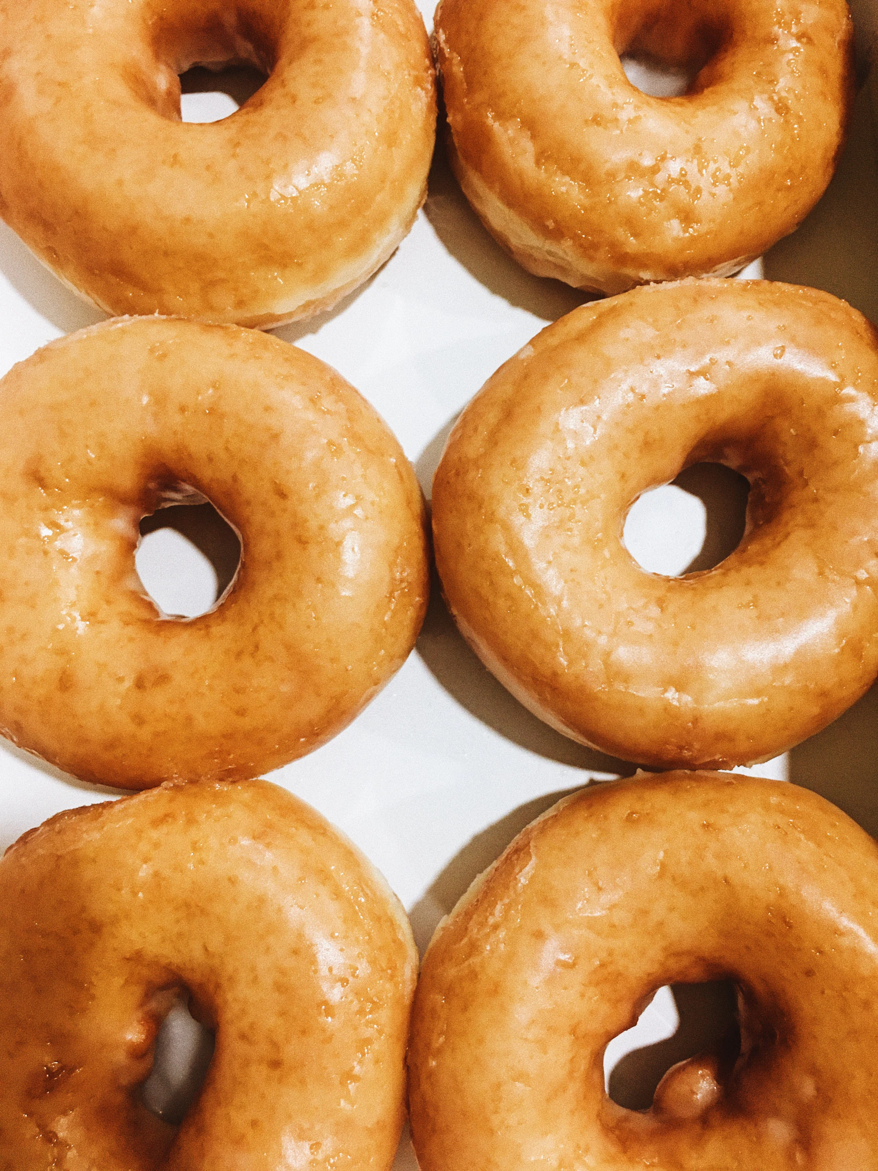 Six classic glazed ring donuts in a white box, seen from above