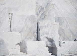 Large, rectangular slabs of white marble stacked together, showcasing natural veins and patterns in the stone surface, set against a bright and possibly harsh lighting condition.