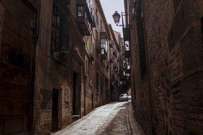 cars parked on side of the road in between of brown concrete buildings during daytime