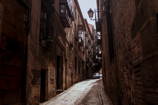 cars parked on side of the road in between of brown concrete buildings during daytime in Toledo Spain