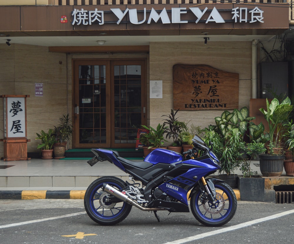 blue and black sports bike parked beside brown concrete building during daytime