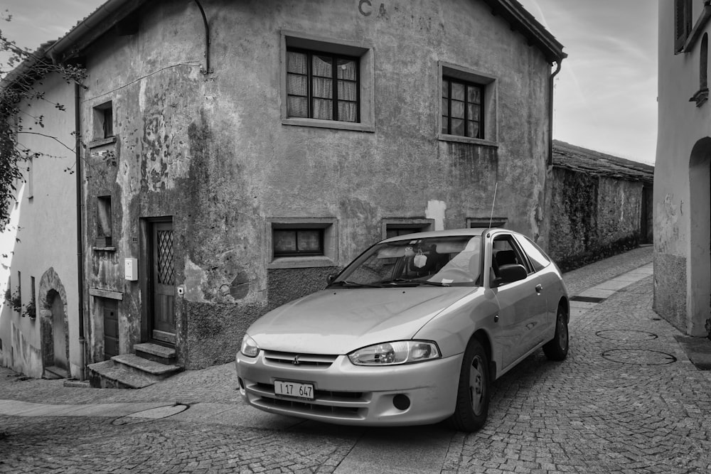 grayscale photo of mercedes benz coupe parked beside concrete building